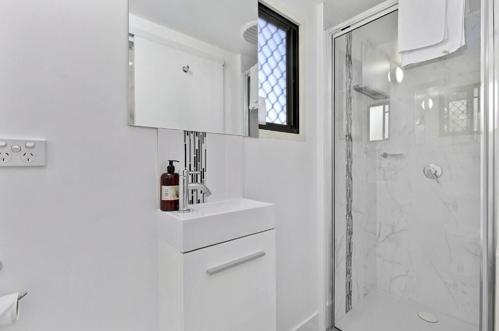 A modern bathroom with a white vanity, a glass shower enclosure, and a window with a geometric pattern.