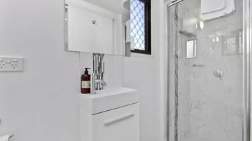 A modern bathroom with a white vanity, a glass shower enclosure, and a window with a geometric pattern.