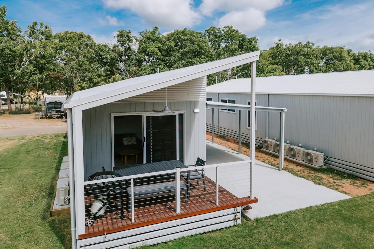 A modern RV with a covered porch and a sliding door leading to a living area.