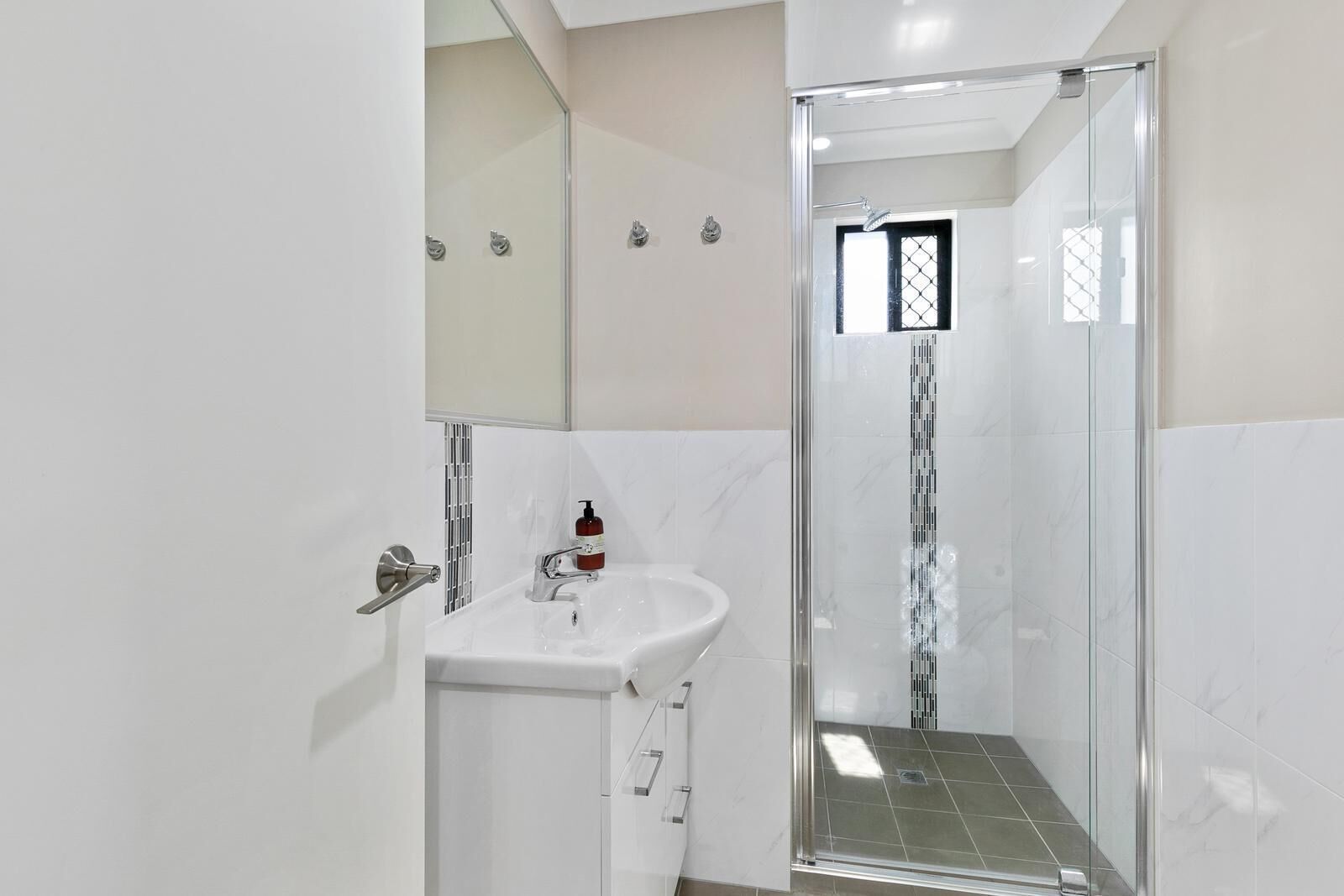 Un baño moderno con ducha de vidrio, lavamanos blanco y espejo.