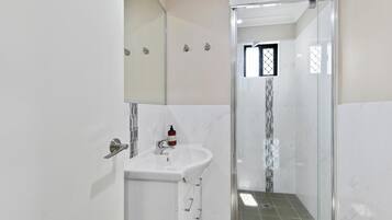Un baño moderno con ducha de vidrio, lavamanos blanco y espejo.