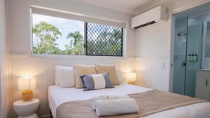 A neatly made bed with a striped blanket, two bedside lamps, and a window with a view of trees. - Ingenia Holidays Townsville (Deeragun)