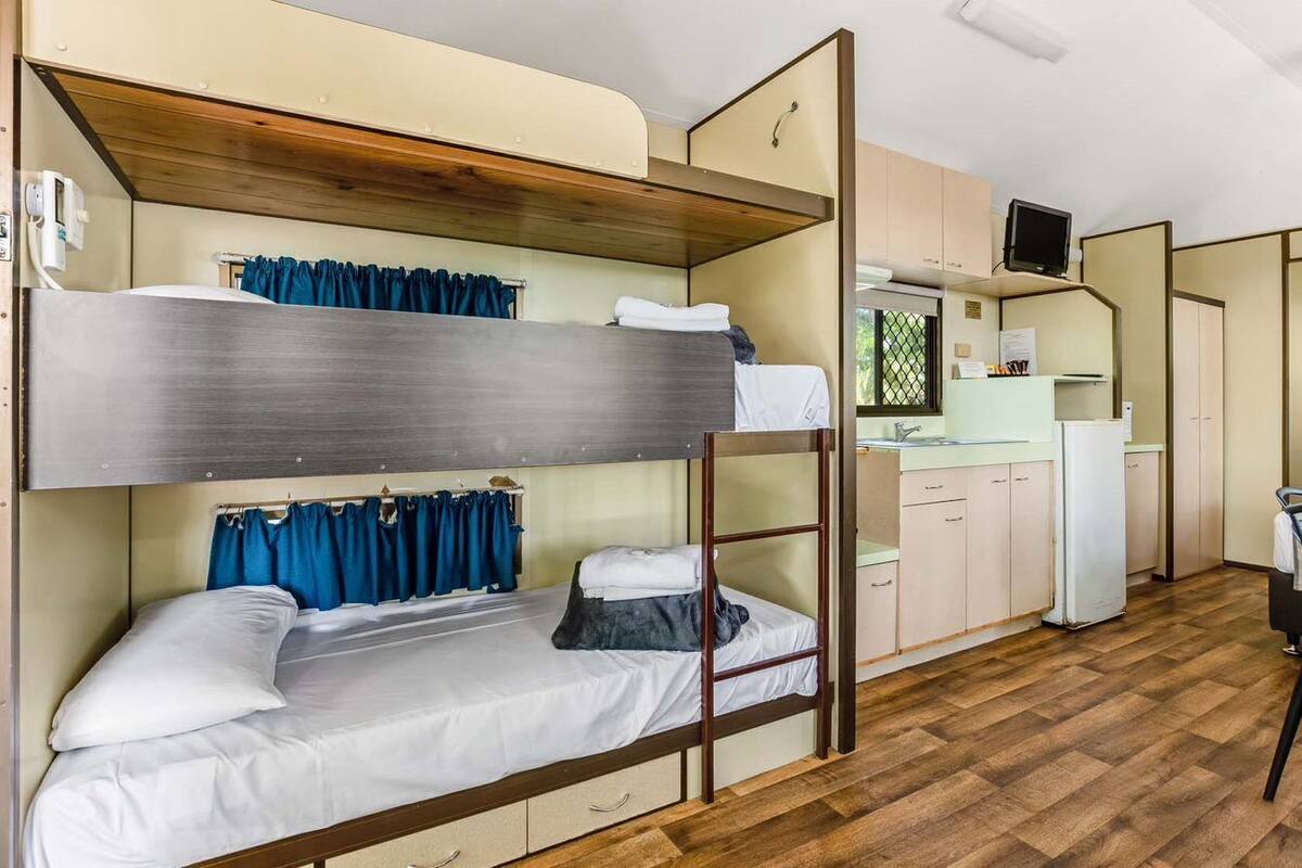 A bunk bed room with a kitchen area, including a refrigerator, a sink, and a television.