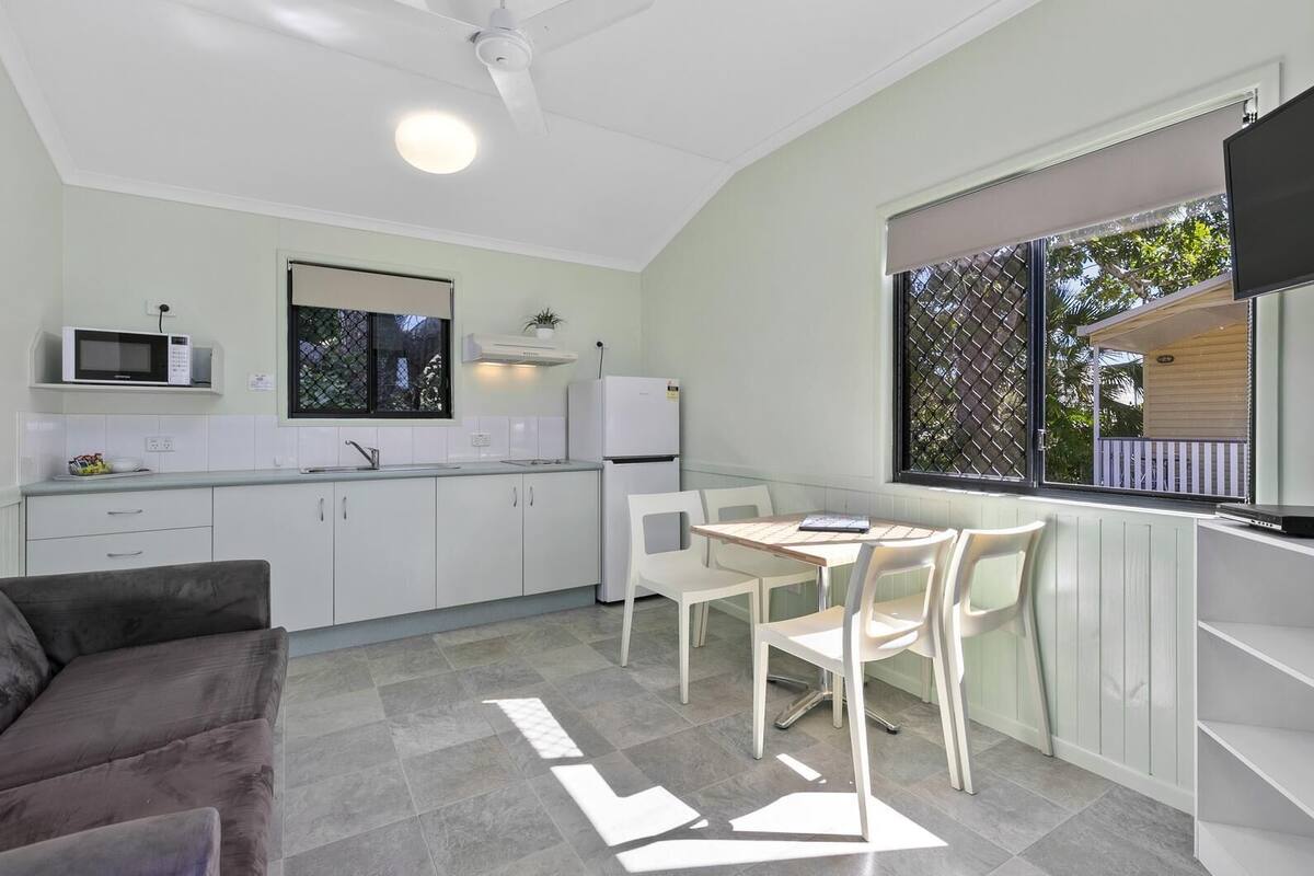 A compact kitchen with white cabinets, a microwave, a refrigerator, and a dining area with a table and chairs.