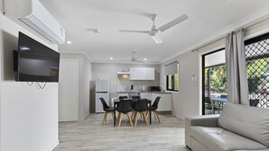 A modern living room with a sofa, dining area with chairs, a TV, and a kitchen with cabinets and appliances. - Ingenia Holidays Townsville (Deeragun)