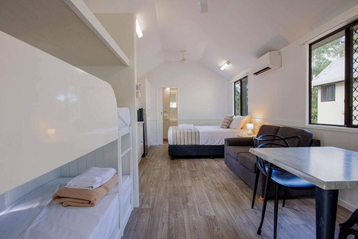 A compact room with a bed, a sofa, a table, and a window.