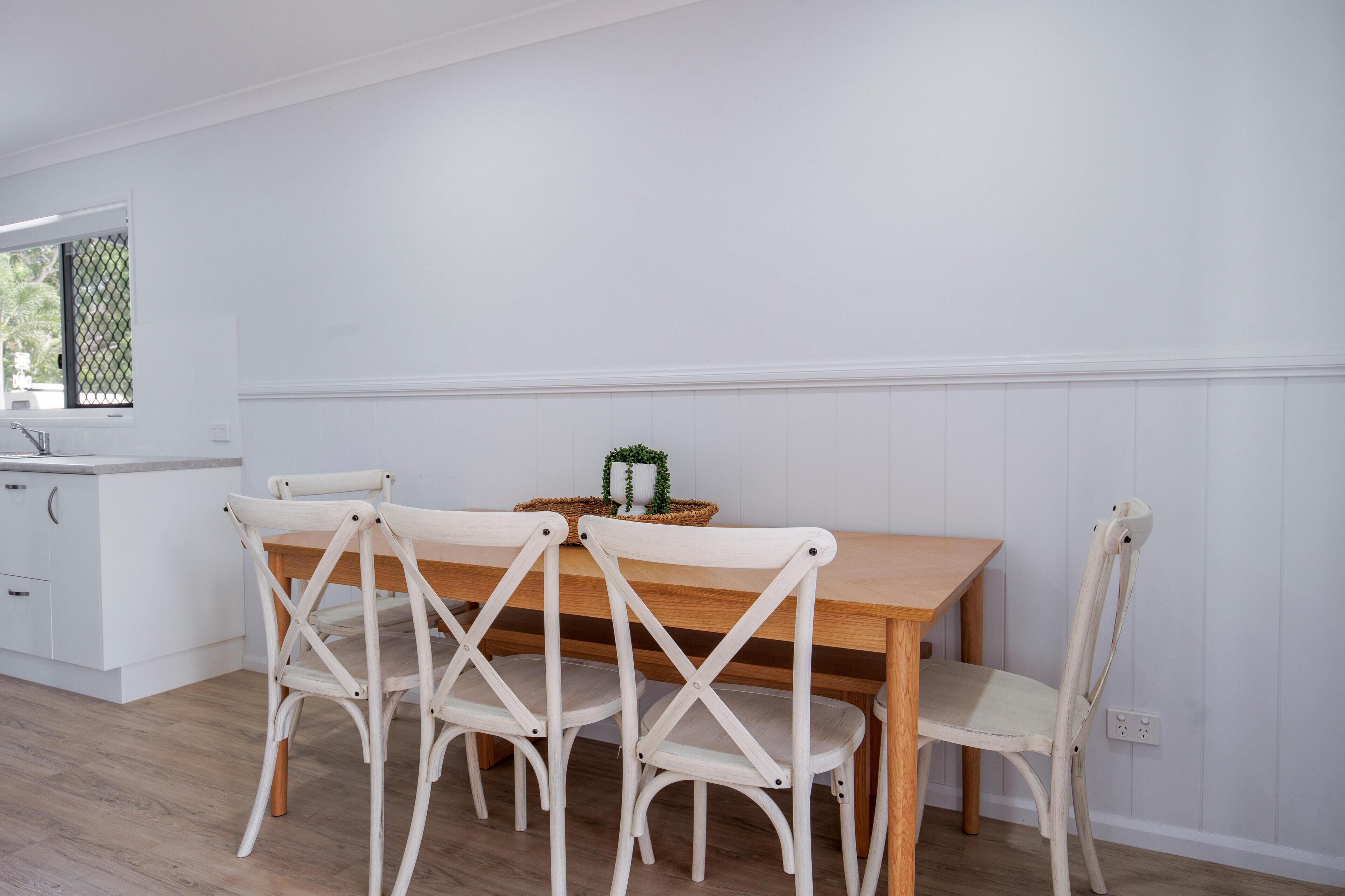 A dining area with a wooden table and four white chairs with a crisscross back design.