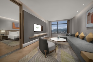 Habitación de hotel moderna con vista a la ciudad, un sofá, una silla, un televisor y una cama.