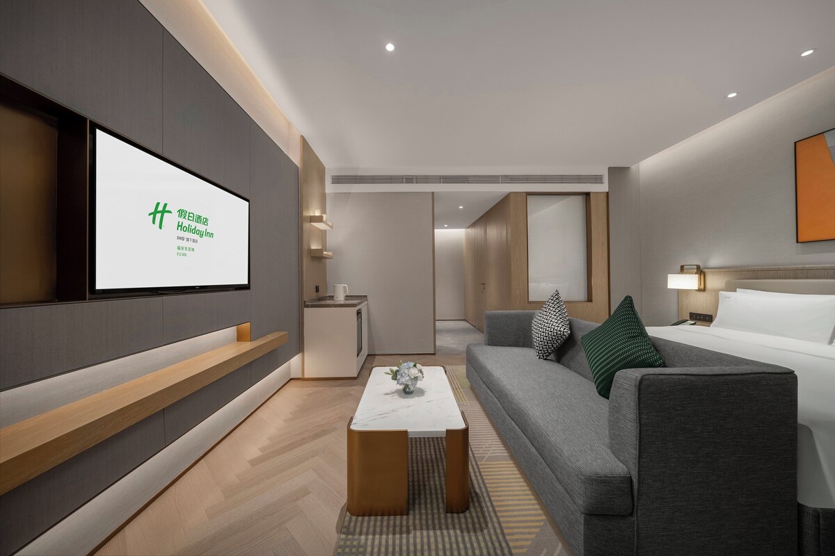 A modern hotel room with a flat-screen TV, a sofa, a coffee table, and a bed.