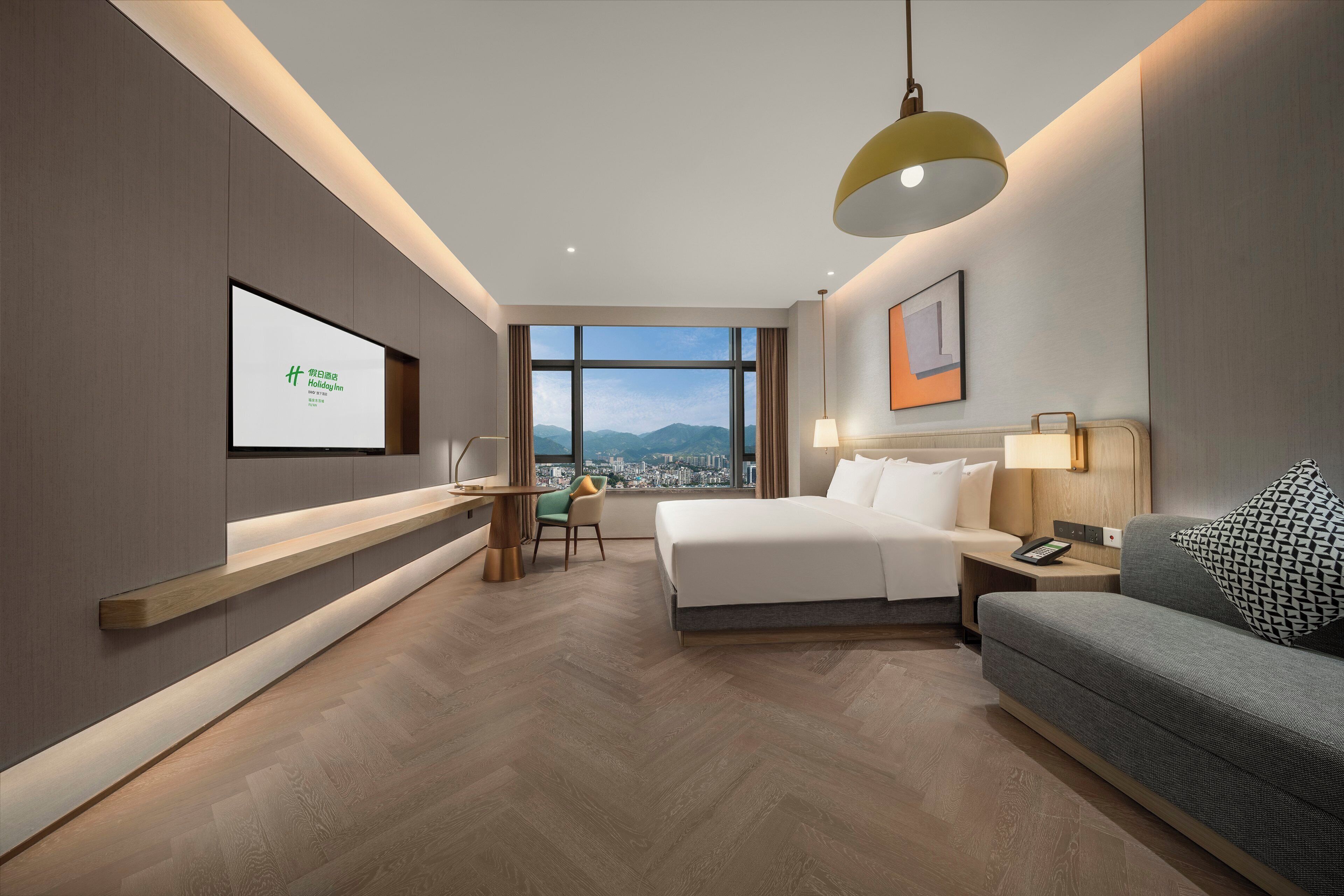 A hotel room with a bed, a sofa, a desk, and a TV screen displaying a hotel name.