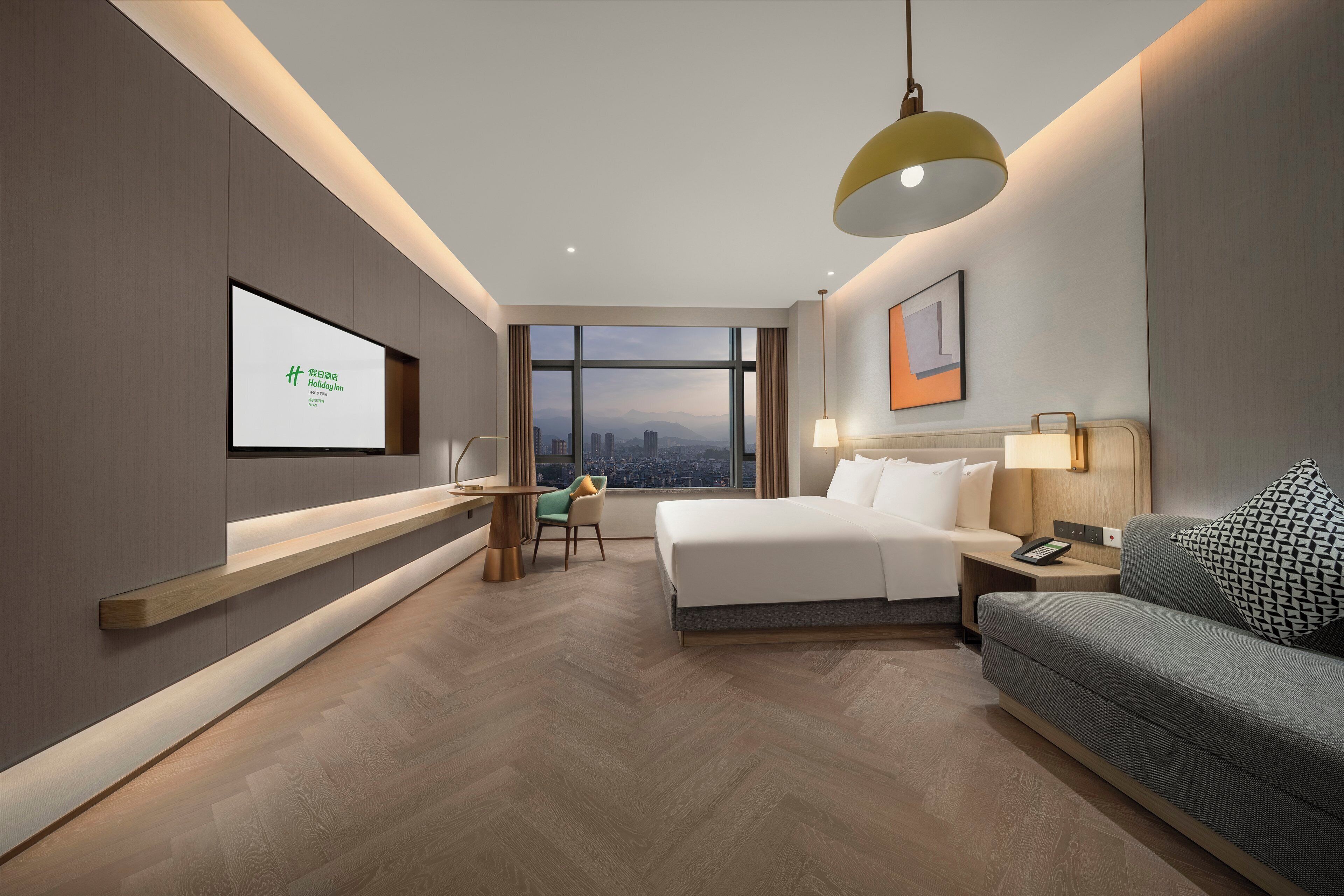 Ein modernes Hotelzimmer mit einem Bett, einem Schreibtisch, einer Couch und einem großen Fenster mit Blick auf die Stadt.