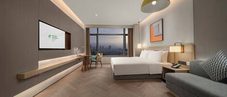 Habitación de hotel moderna con cama, escritorio, sofá y un amplio ventanal con vistas a la ciudad.