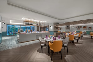 A modern restaurant with a central bar area, multiple dining tables with chairs, and a patterned floor.