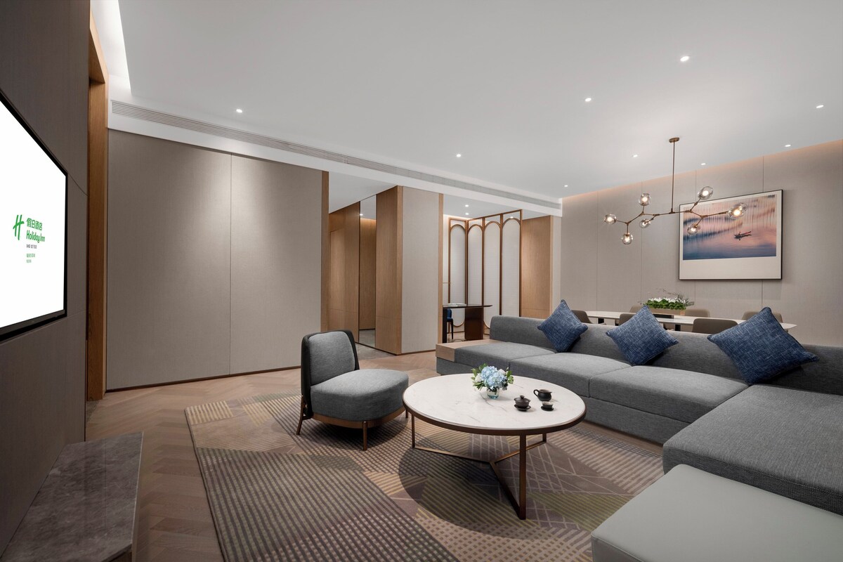 A modern living room with a sofa, armchairs, a coffee table, and a TV screen displaying a logo.