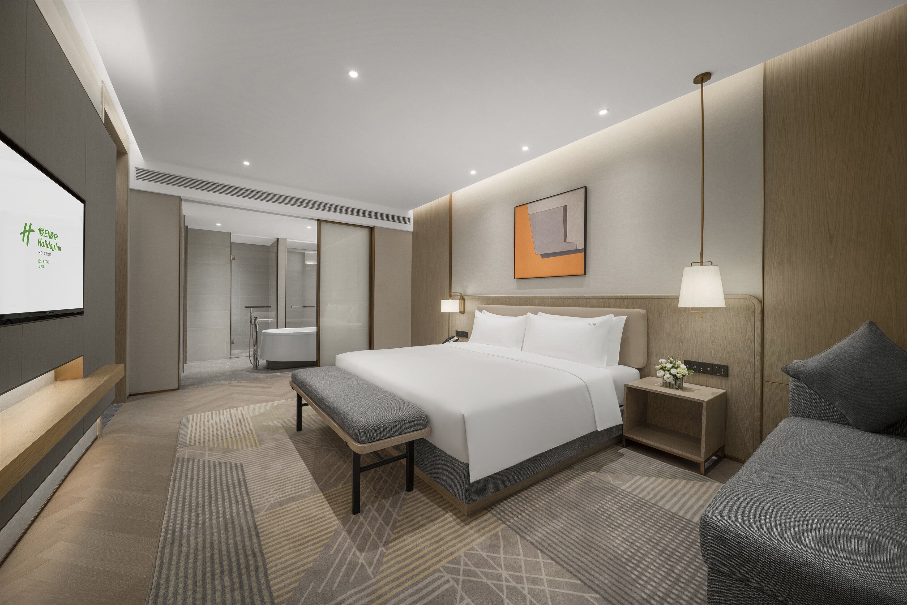 A modern hotel room with a large bed, bedside tables, a bench, and a small sofa.