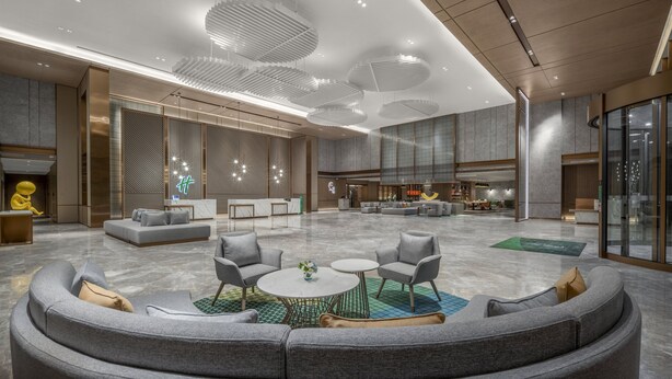 Een ruime lobby met een centraal zitgedeelte, een receptiebalie en een groot raam dat uitzicht biedt op het interieur.