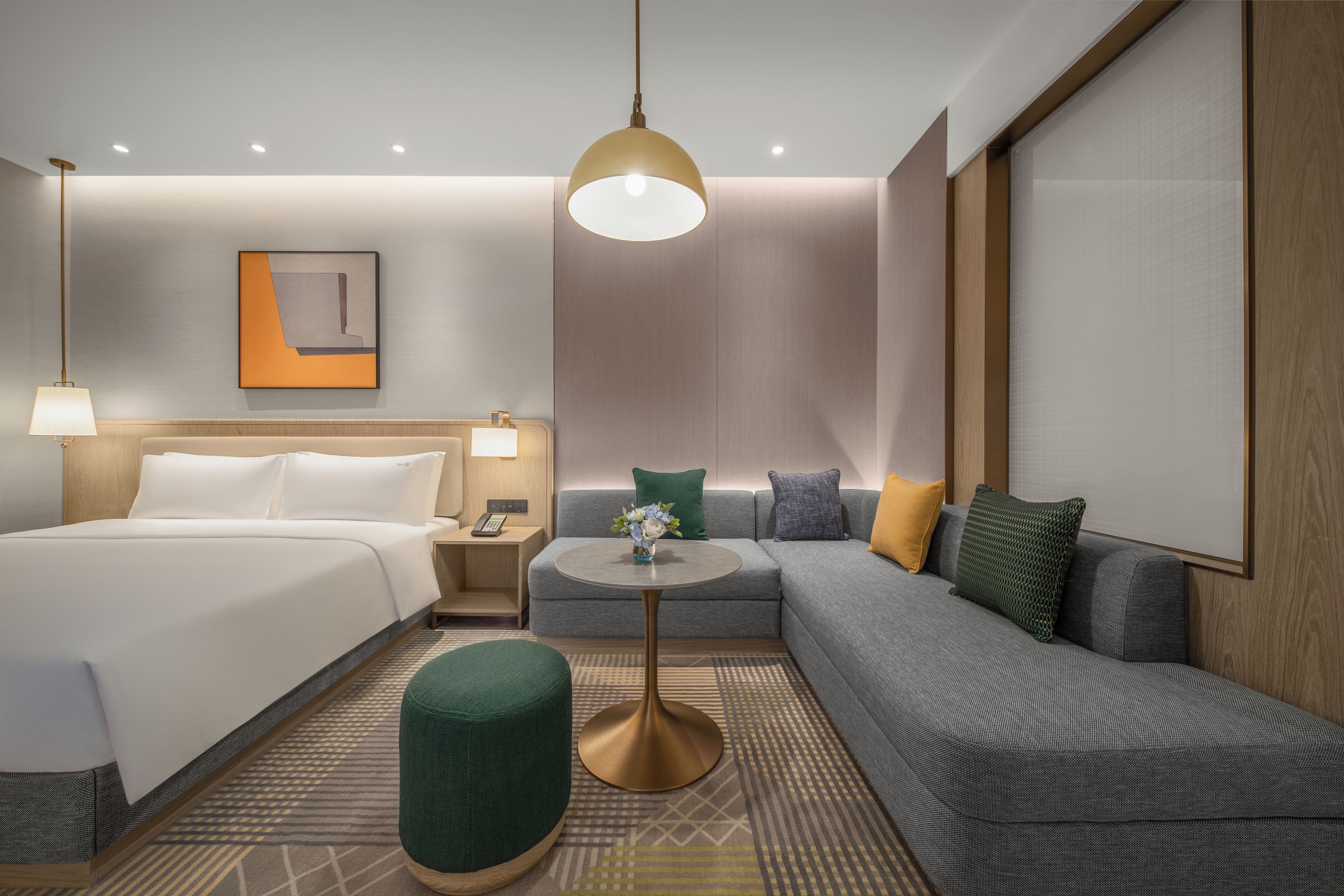 A modern hotel room with a bed, a sofa, a small table, and a lamp.