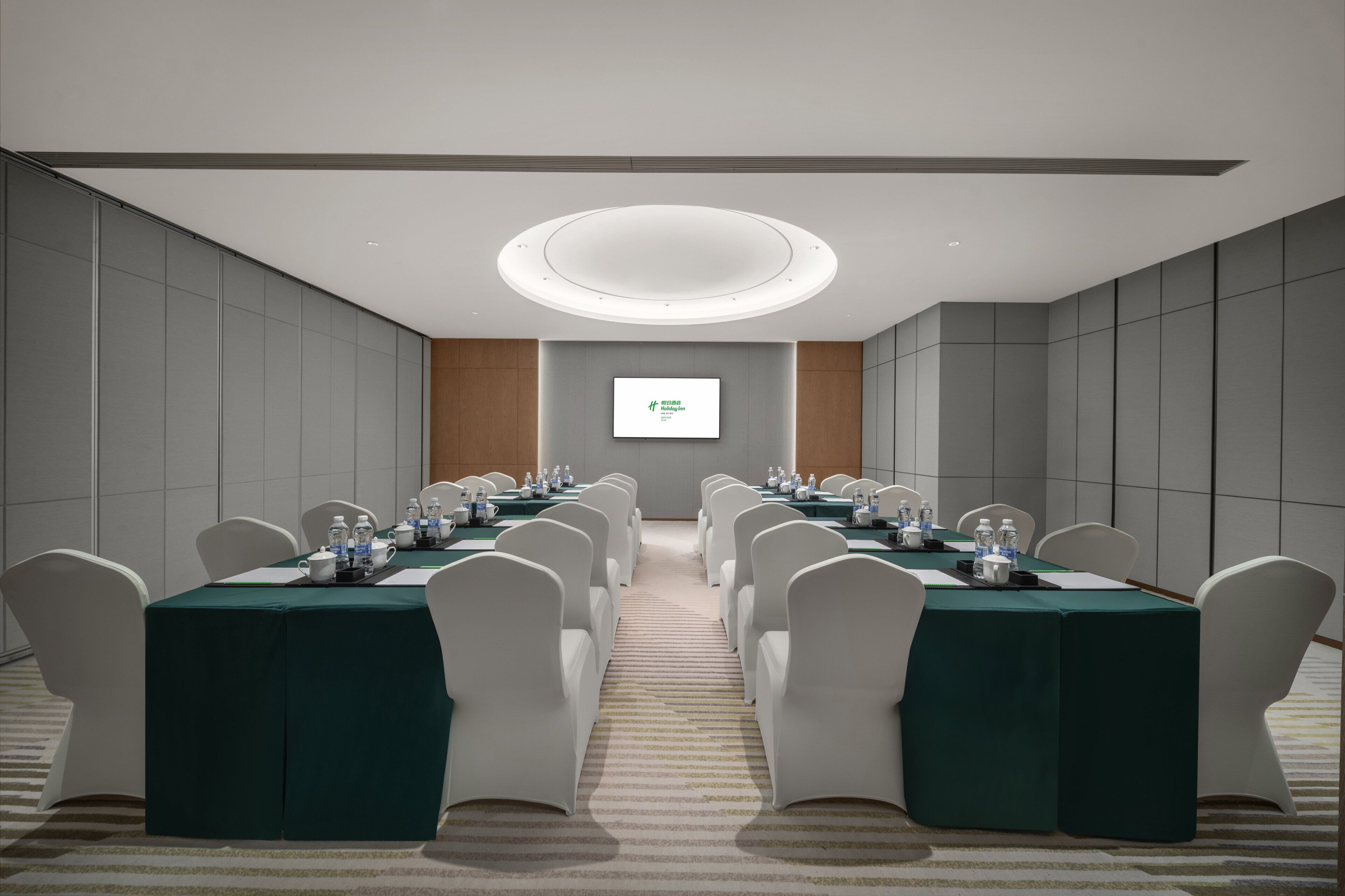 A conference room with a long table, white chairs, and a projector screen on the wall.