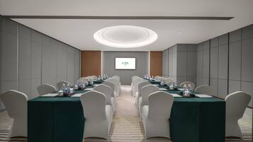 A conference room with a long table, white chairs, and a projector screen on the wall.