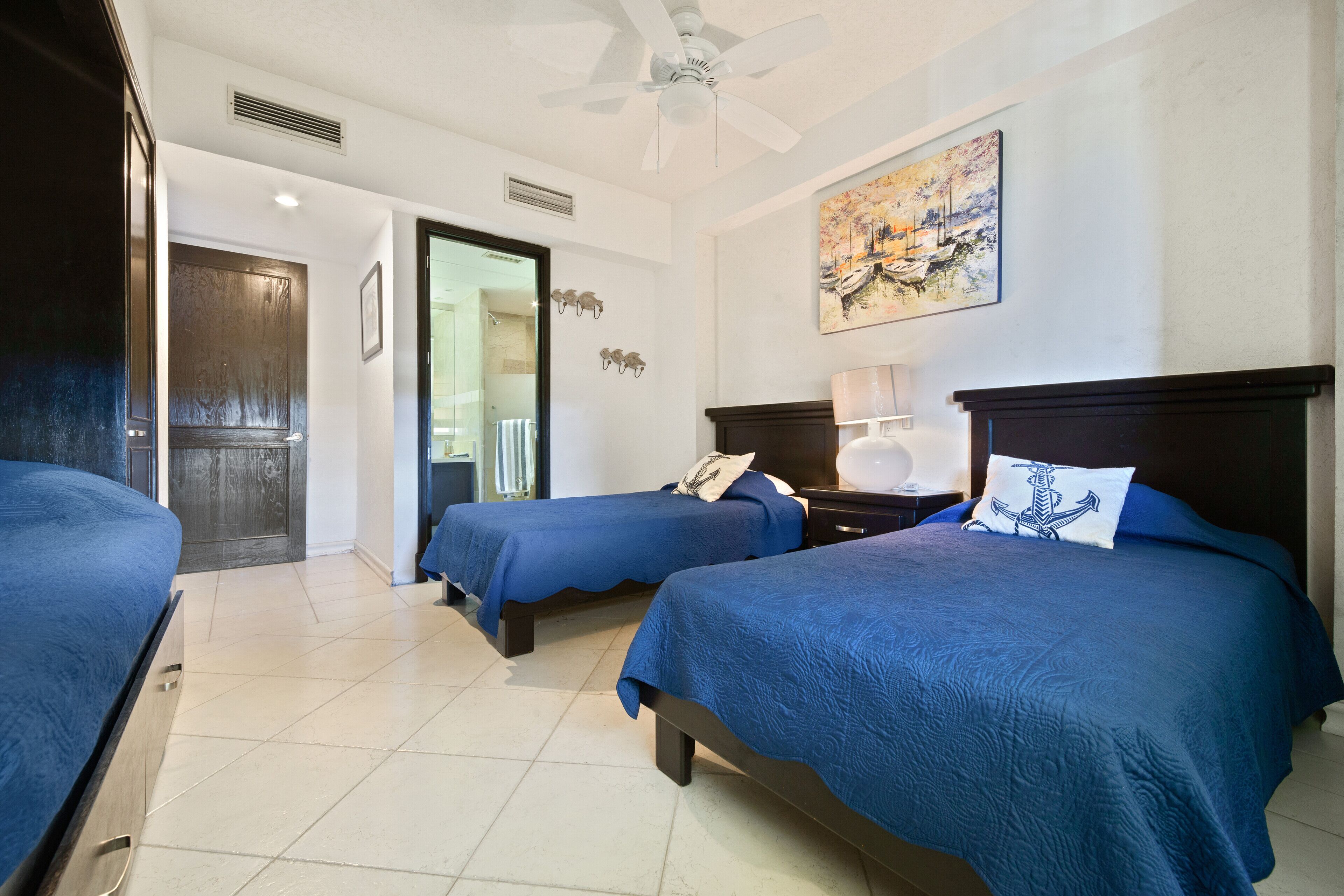 A hotel room with two beds, a ceiling fan, a painting, and a door leading to another room.