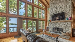A spacious living room with a stone fireplace, large windows, and a view of the lake. - Aspen Shores by Innsbrook Vacations! (Innsbrook)