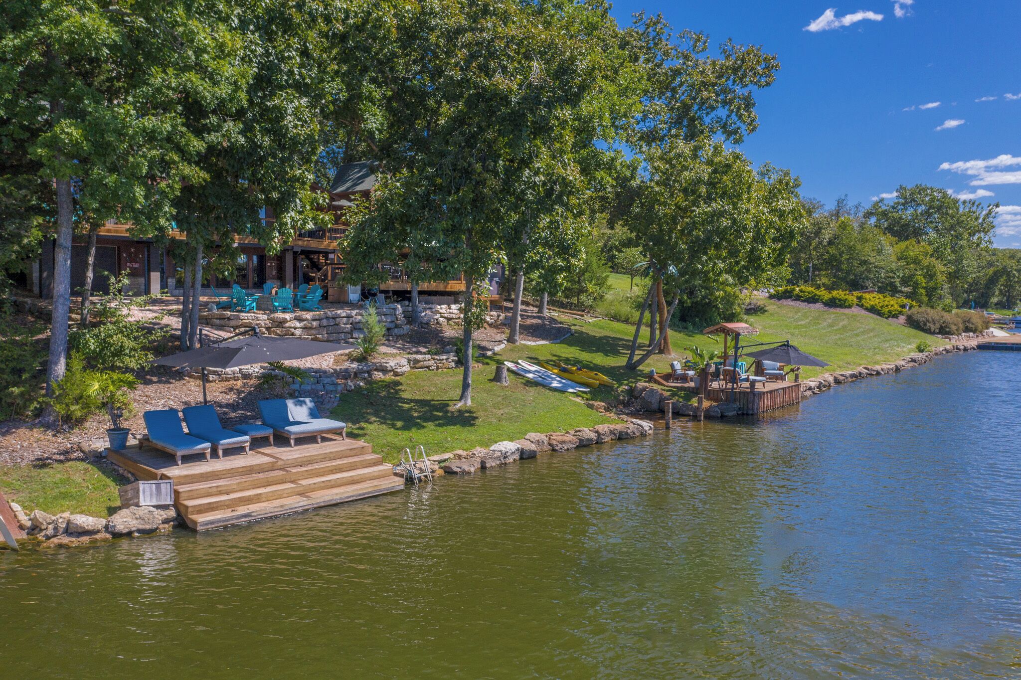A lakeside property with a dock, lounge chairs, and a covered seating area.