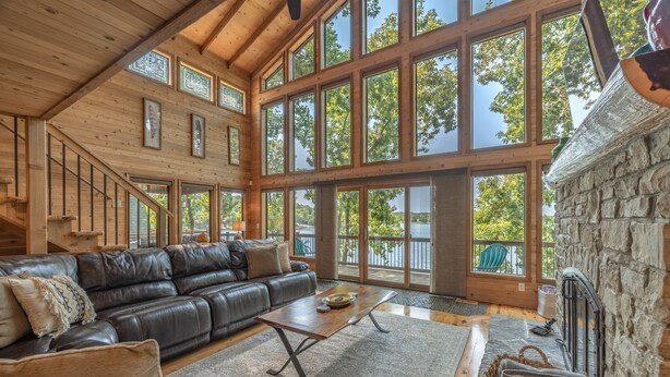 A spacious living room with a leather sofa, a coffee table, and a stone fireplace. Large windows offer views of the outdoors. - Aspen Shores by Innsbrook Vacations! (Innsbrook)