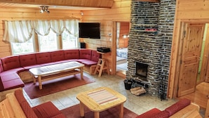 A cozy log cabin interior with a stone fireplace, a red sofa, a wooden coffee table, and a television. - Porukka 2 by Interhome (Kittilä)