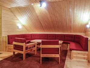 A cozy log cabin interior with a wooden ceiling, a red upholstered bench, and a wooden table.