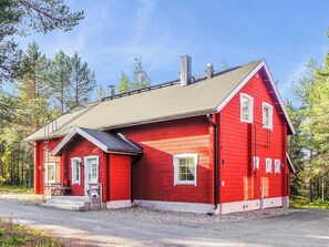 Et rødt træhus med skråt tag, skorsten og en lille veranda med bænk.