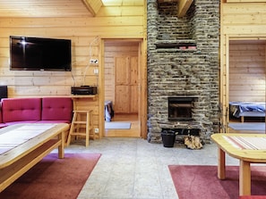 A cozy cabin interior with a stone fireplace, wooden walls, a flat-screen TV, and a red sofa.