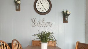 Un comedor con una mesa de madera, cuatro sillas de madera, una planta en maceta, un reloj de pared y un cartel que dice 'Father'.