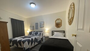 Habitación de hotel con dos camas, un armario de madera, una mesita con una lámpara y un espejo en la pared.