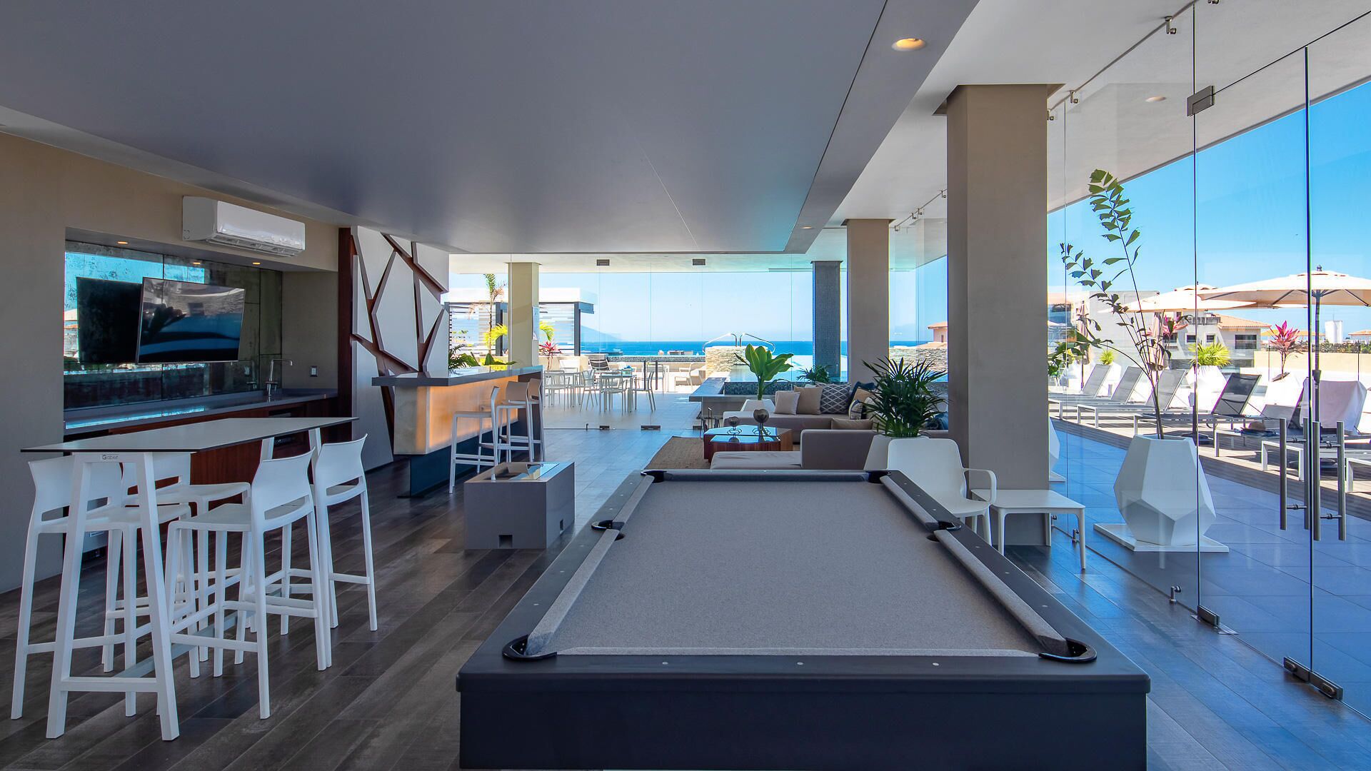 Un espace piscine moderne comprenant une table de billard, un bar et des sièges avec vue sur la mer.