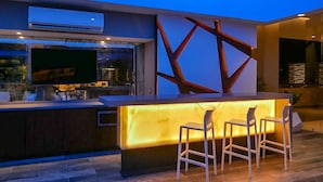 Un espace bar moderne avec une cloison en verre, un téléviseur à écran plat et deux tabourets de bar.