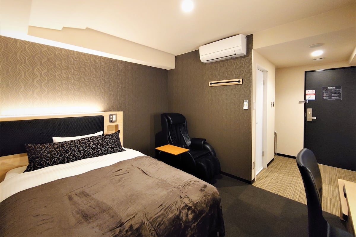 Een hotelkamer met een bed, een bureau, een stoel, een airconditioning en een deur.
