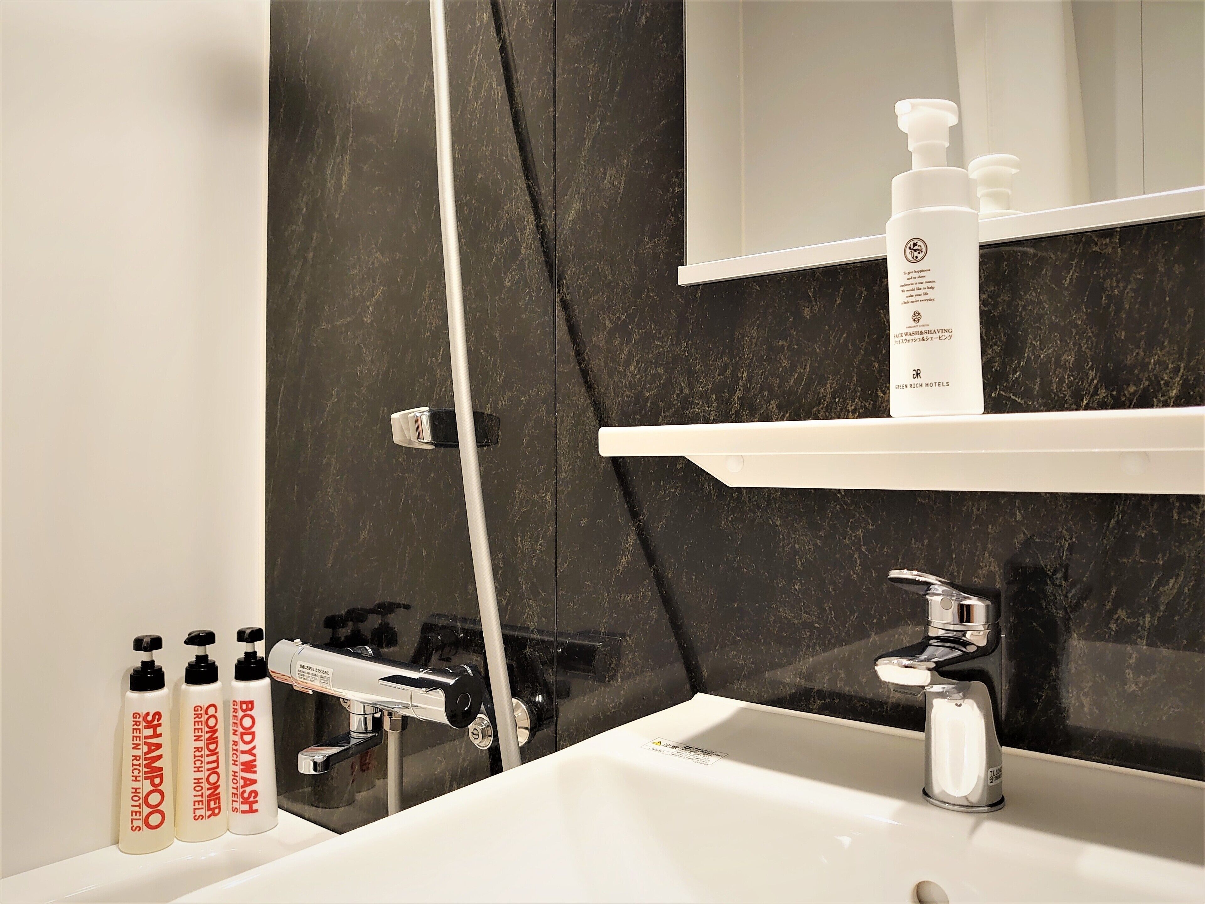 Un baño con pared de mármol negro, un lavamanos blanco y tres botellas de champú y acondicionador.