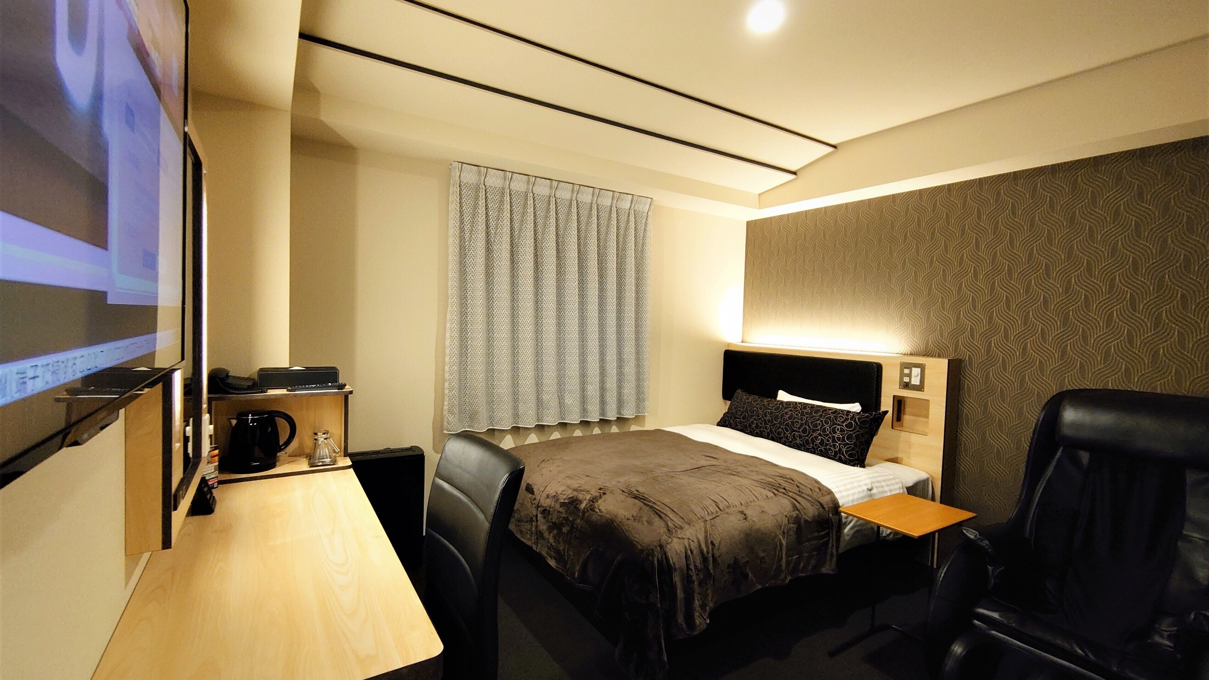 A hotel room with a bed, a desk with a computer, a chair, and a TV screen.