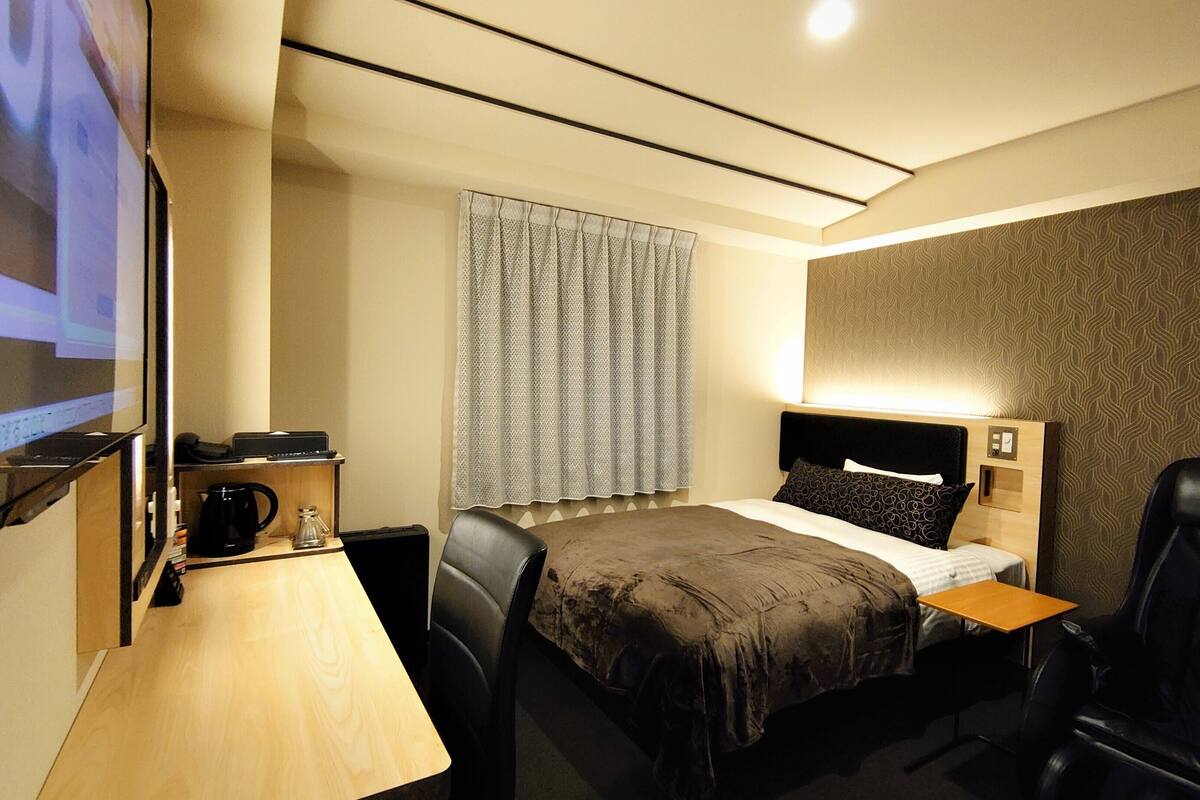 Een hotelkamer met een bed, een bureau met een computer, een stoel en een televisiescherm.
