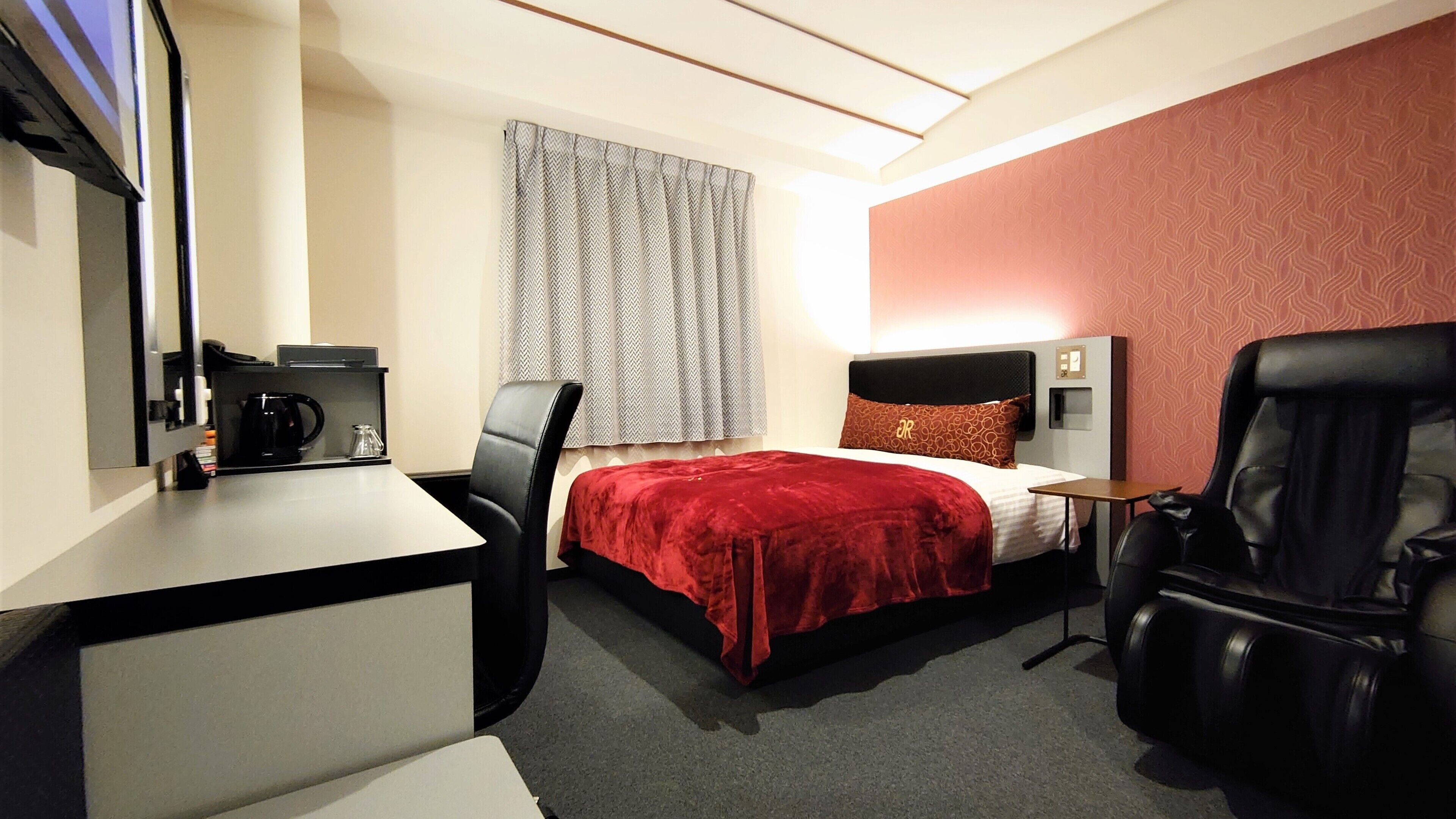 A hotel room with a bed, a desk, a chair, and a small table.