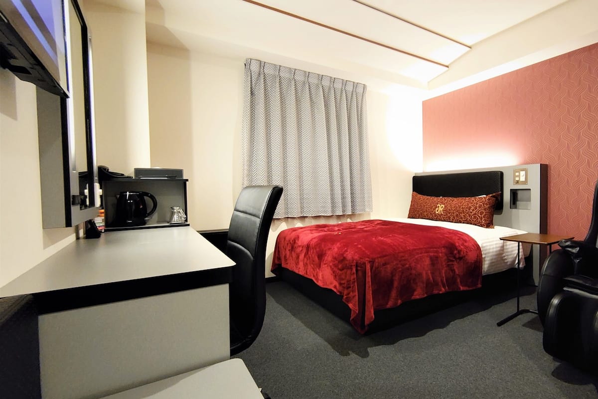 Een hotelkamer met een bed, een bureau, een stoel en een klein tafeltje.