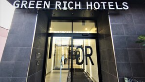 La entrada a Green Rich Hotels con un diseño moderno, que incluye una puerta de cristal y un letrero metálico arriba.