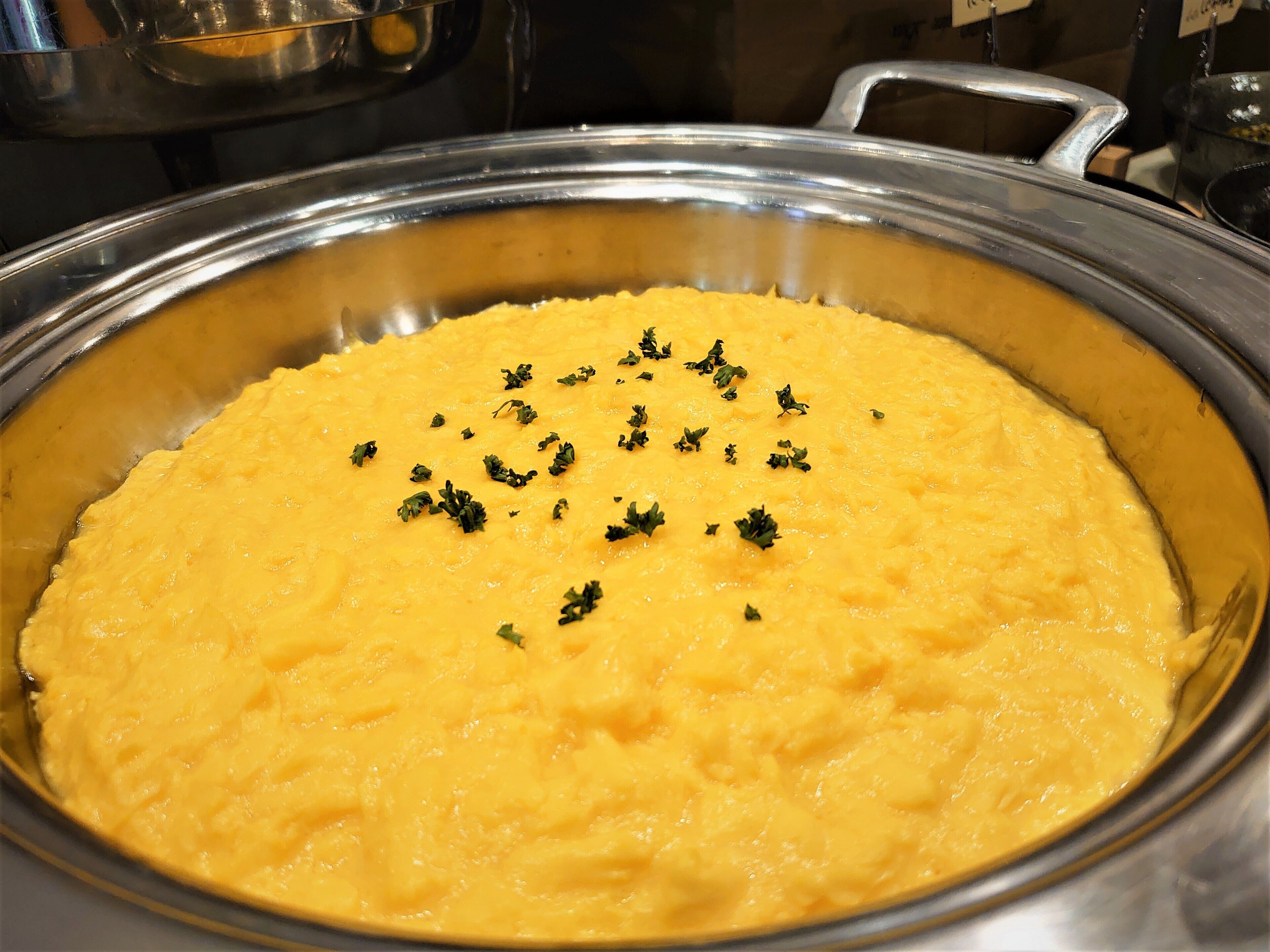 Uma panela de metal grande cheia de um líquido amarelo, possivelmente alimento, decorada com ervas verdes.