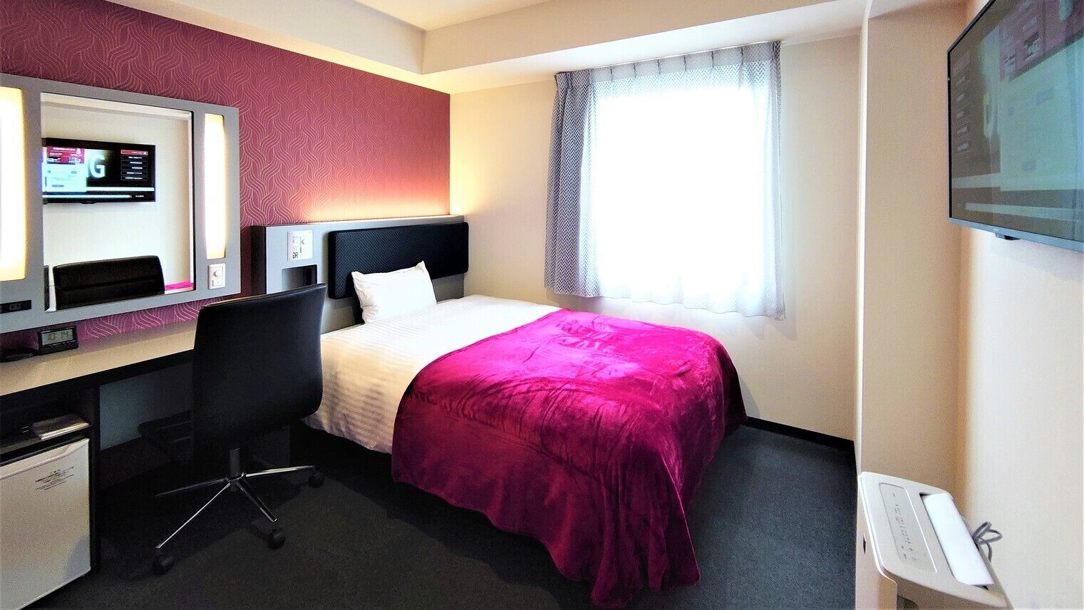 Een hotelkamer met een bed, een bureau met een computer, een stoel, een televisie en een raam met gordijnen.