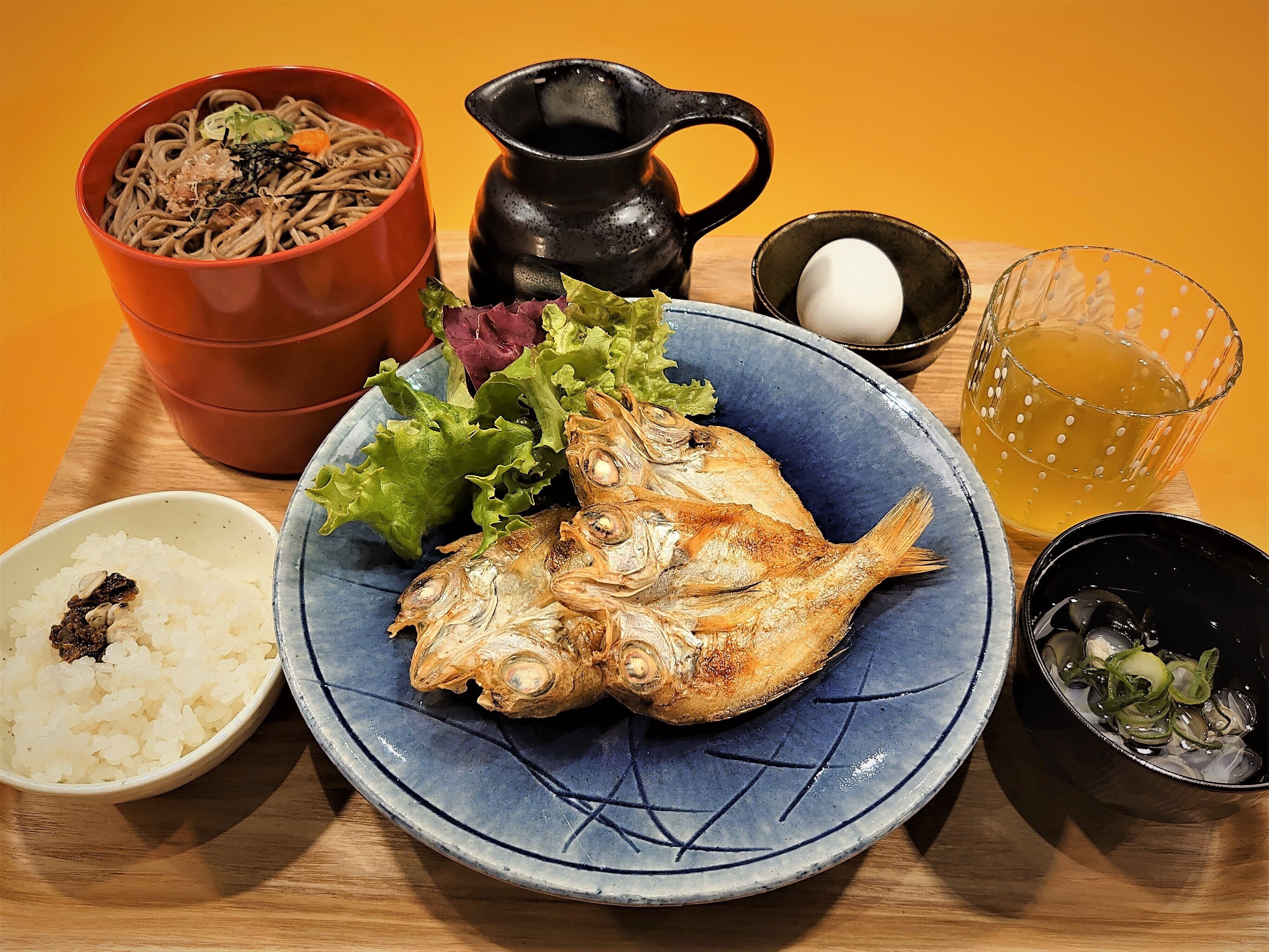 A meal with a fish, rice, noodles, and a pitcher of tea.