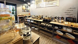 Un café con un panel de menú que enumera artículos como café, verduras frescas y sándwiches. Se observan varios equipos de cocina y una exhibición de platos en estantes.