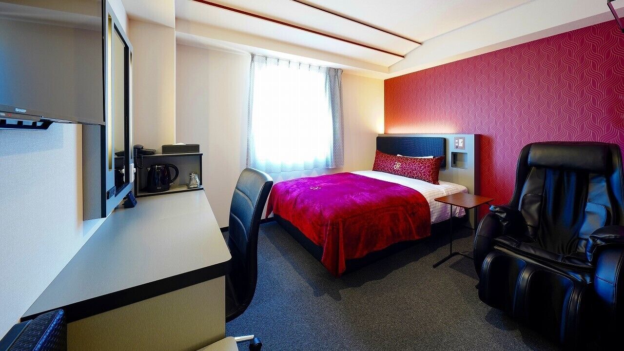 Een hotelkamer met een bed, een bureau met een computer, een stoel, een massagestoel en een televisie.