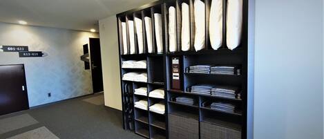 Un vestíbulo de hotel con mostrador de recepción, un teléfono en la pared y un armario con toallas y batas dobladas.
