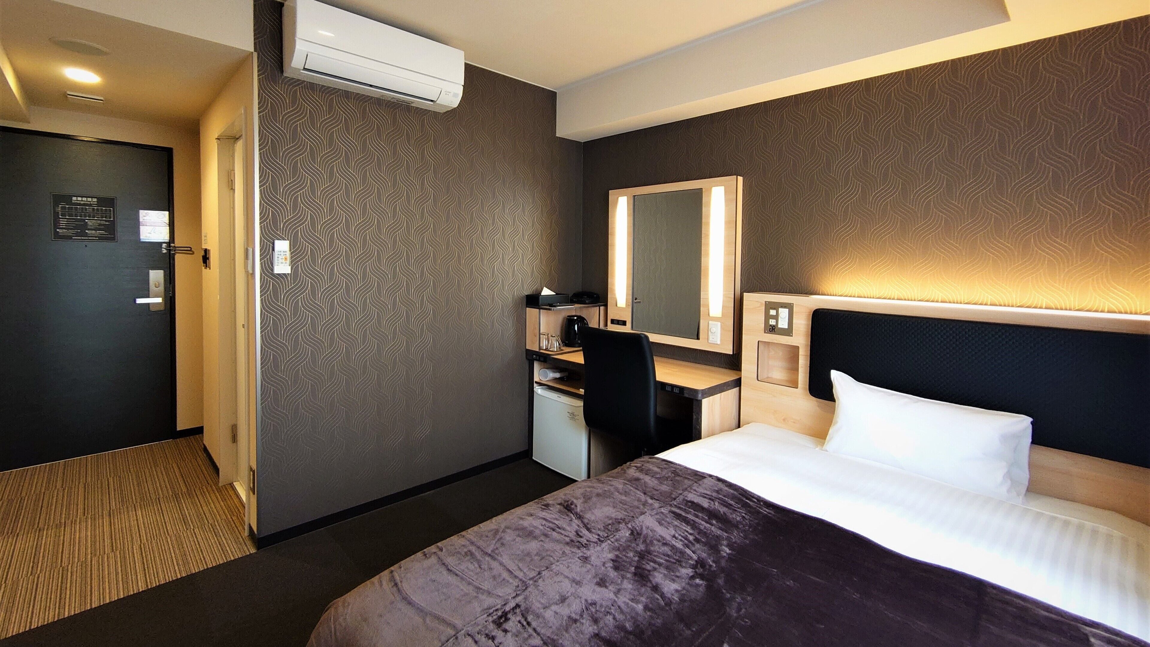 A hotel room with a bed, desk, chair, and a large mirror.