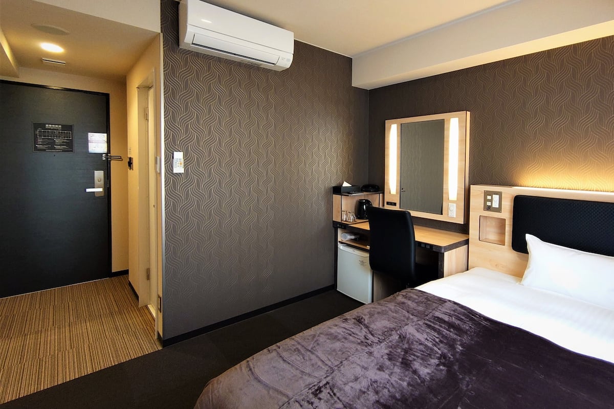 Een hotelkamer met een bed, bureau, stoel en een grote spiegel.